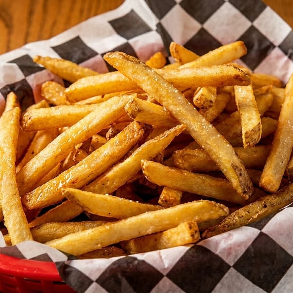 Golden french fries in a red basket lined with black and white checkered paper.