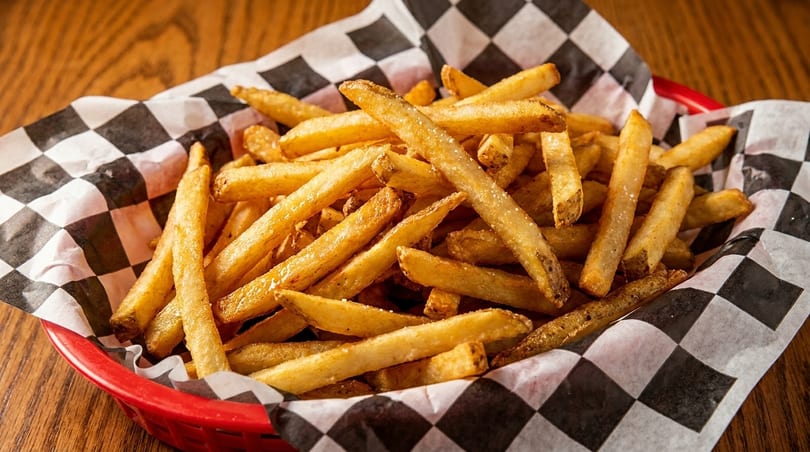 Golden french fries in a red basket lined with black and white checkered paper.